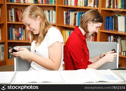 Teenage girls texting in the school library, instead of studying.