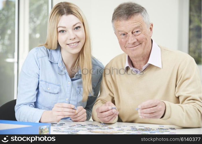 Teenage Granddaughter Helping Grandfather With Jigsaw Puzzle