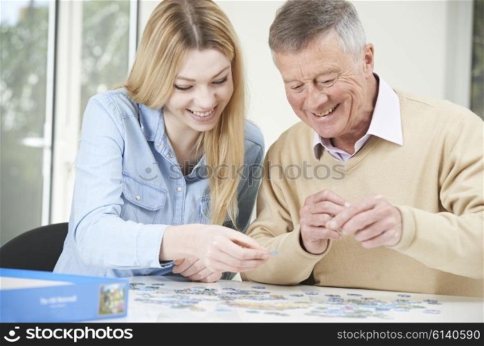 Teenage Granddaughter Helping Grandfather With Jigsaw Puzzle