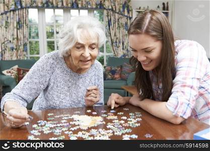 Teenage Granddaughter Helping Grandmother With Jigsaw Puzzle