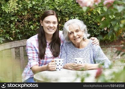 Teenage Granddaughter Relaxing With Grandmother In Garden