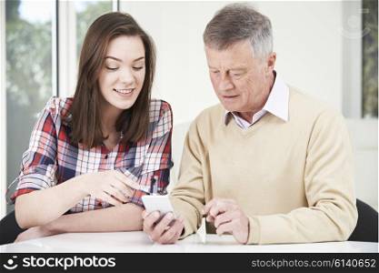 Teenage Granddaughter Showing Grandfather How To Use Mobile Phone