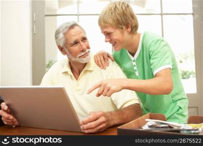 Teenage Grandson Helping Grandfather To Use Laptop At Home