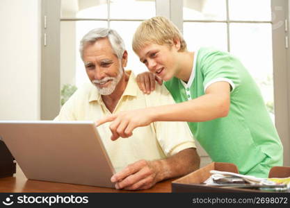 Teenage Grandson Helping Grandfather To Use Laptop At Home