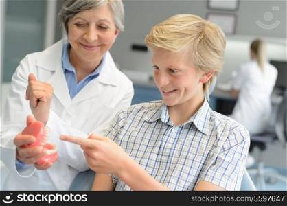 Teenage patient boy dentist woman show dentures teeth at dental surgery