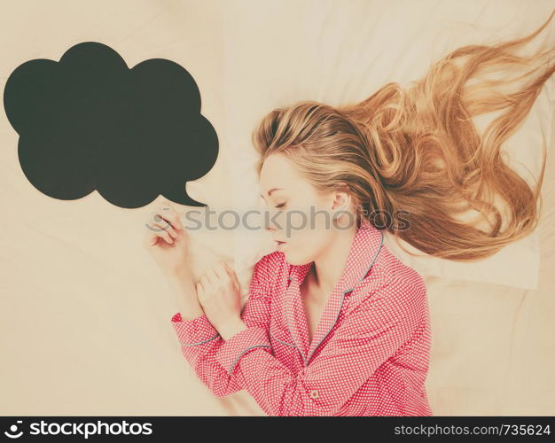 Teenage sleepwear fashion concept. Young woman lying on bed wearing cute pink pajamas, black thinking or speech bubble next to her.. Young woman lying on bed wearing pajamas