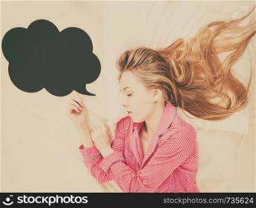 Teenage sleepwear fashion concept. Young woman lying on bed wearing cute pink pajamas, black thinking or speech bubble next to her.. Young woman lying on bed wearing pajamas