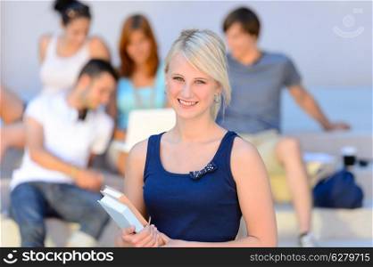 Teenage student girl smiling holding books friends in background summer