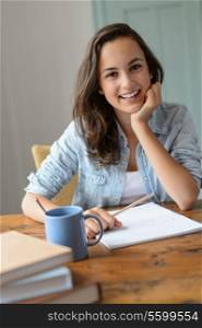 Teenage student girl studying at home smiling leaning against table