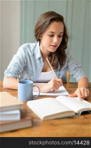 Teenage student girl studying book at home sitting behind table