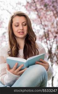 Teenage student reading book outside near blossoming tree spring