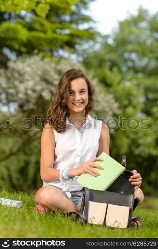 Teenage student woman sitting grass putting books in school bag