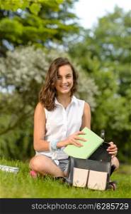 Teenage student woman sitting grass putting books in school bag