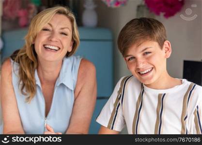 Teenage teen boy son laughing in a kitchen with his mother out of focus behind him