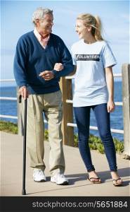 Teenage Volunteer Helping Senior Man Walking Along Path By The Sea
