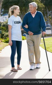 Teenage Volunteer Helping Senior Man Walking Through Park