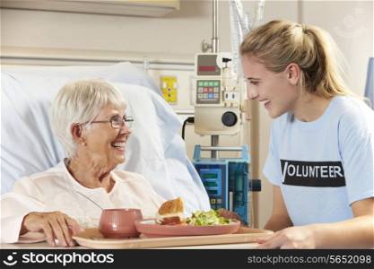 Teenage Volunteer Serving Senior Female Patient Meal In Hospital Bed
