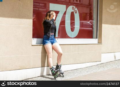 Teenage woman girl riding roller skates during summertime showing sale symbol on window.. Woman wearing roller skates next to sale