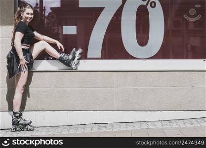 Teenage woman girl riding roller skates during summertime showing sale symbol on window.. Woman wearing roller skates next to sale