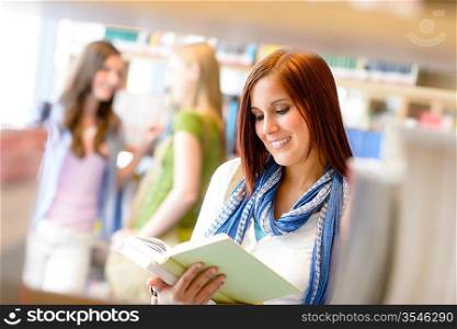 Teenage woman reading book studying among library shelves