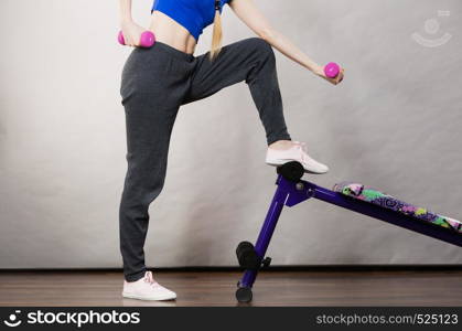 Teenage young woman working out at home with small light dumbbells. Training at home, being fit and healthy, presenting sit ups bench. Teenage woman working out at home with dumbbell