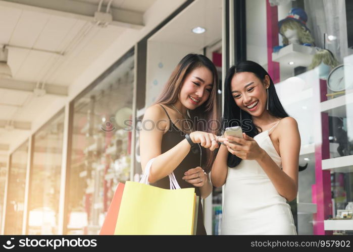 Teenager asian woman standing at store front with happy watching smart phone at shopping mall center.