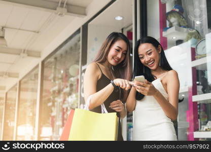 Teenager asian woman standing at store front with happy watching smart phone at shopping mall center.