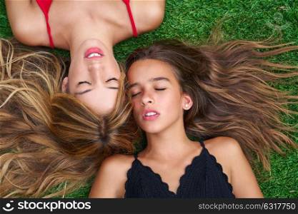 Teenager best friends girls lying down on backyard turf grass