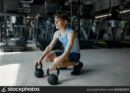 Teenager boy preparing for weightlifting sitting with kettlebell over sport gym hall background. Teenager boy preparing for weightlifting sitting with kettlebell