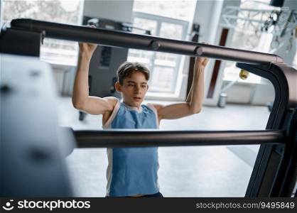 Teenager boy pulling up on crossbar closeup shot over gym background. Sports hobby for children. Teenager boy pulling up on crossbar closeup shot over gym background