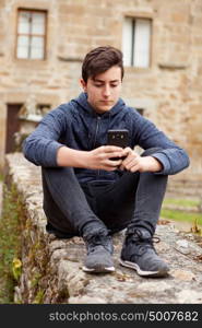 Teenager boy sitting in the street with a stone house of background