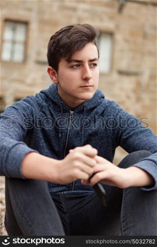 Teenager boy sitting in the street with a stone house of background