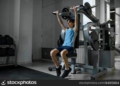 Teenager boy training arms, chest, shoulders and back on exercise machine. Bodybuilding for children concept. Teenager boy training arms, chest, shoulders and back on exercise machine