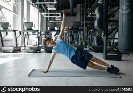 Teenager fitness boy standing in side plank doing core training workout at gym club. Sport and childhood. Teenager fitness boy standing in side plank doing core training workout