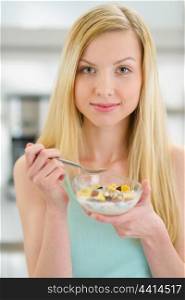 Teenager girl eating flakes with milk in kitchen
