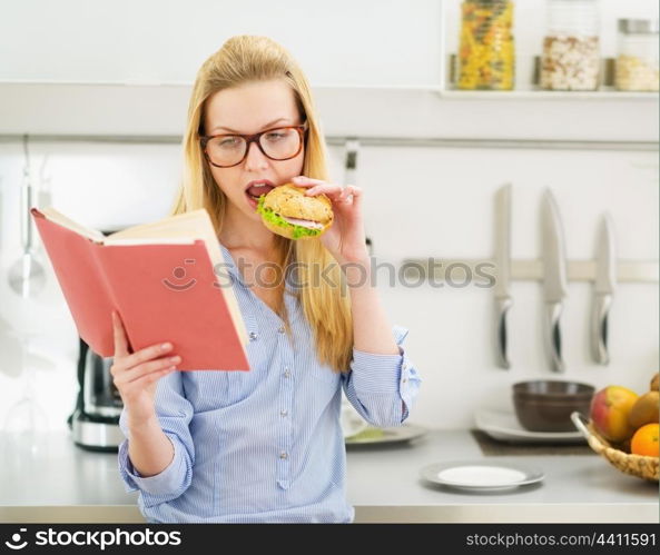 Teenager girl having burger in kitchen while studying