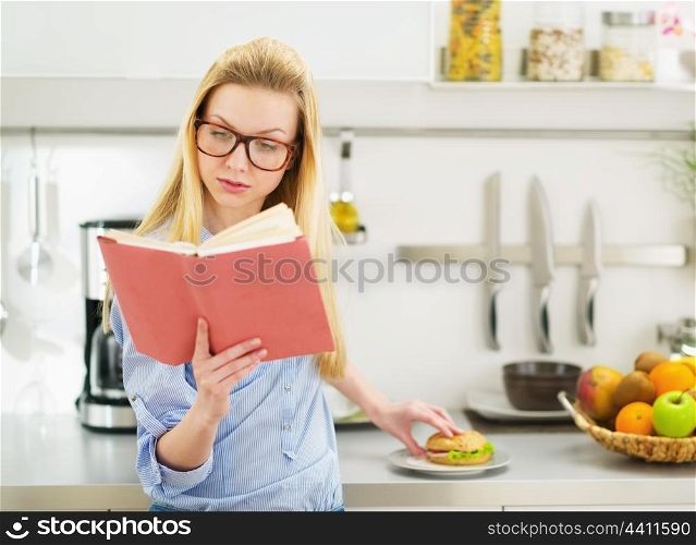 Teenager girl having sandwich in kitchen while studying