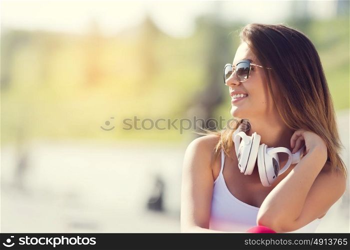 Teenager girl having time in outdoors. Attractive brunette girl in summer park enjoying daytime wearing headphones