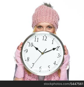 Teenager girl in winter hat and scarf hiding behind clock