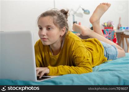teenager girl lying on the bed, using a laptop