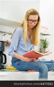 Teenager girl reading book in kitchen