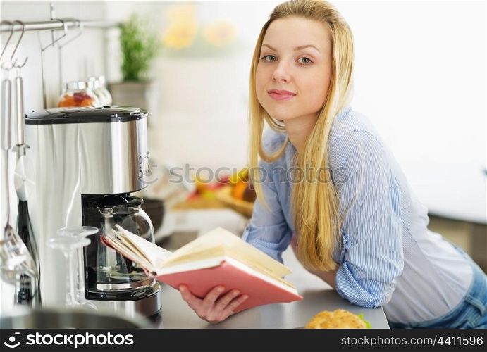 Teenager girl reading book in kitchen