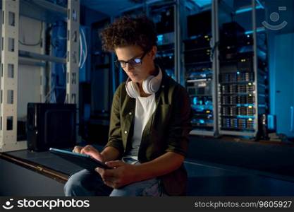 Teenager guy IT technician working on mobile tablet inside server room with supercomputer. Teenager guy IT technician working on tablet inside server room