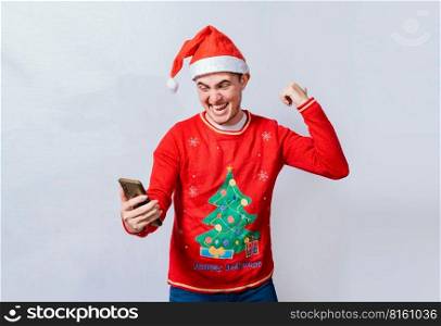 Teenager in christmas hat celebrating a promotion with the cell phone, Happy smiling man in christmas hat holding cellphone celebrating, Happy guy in christmas hat holding cellphone celebrating