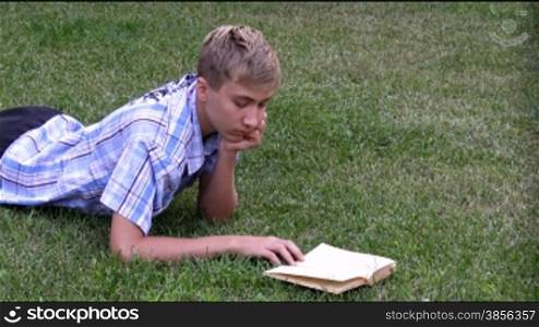 teenager lays on a grass and reads the book.