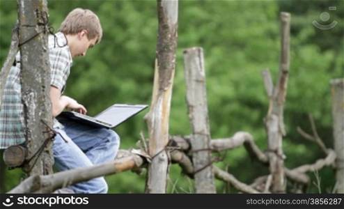 teenager sits on fence with laptop.