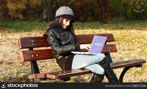 Teenager sitting on bench with laptop in autumn