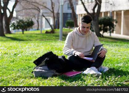 Teenager sitting on the school grass while studying with a book