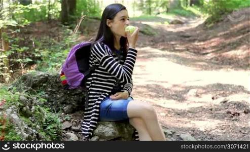 Teenager tourist girl eating apple and enjoying the nature in the forest.