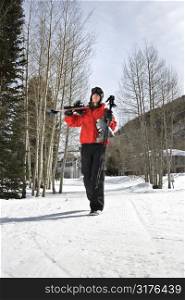 Teenager walking and carrying ski gear.